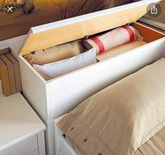 an open drawer on the side of a bed with pillows and blankets in front of it