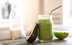 an avocado smoothie in a mason jar with a straw and two limes next to it