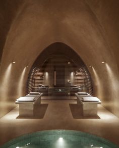 an indoor swimming pool with benches and lights on the walls, in front of a stone wall