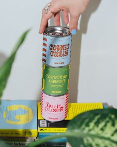 a person holding a can of soda on top of a table next to some books