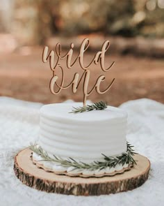 a wedding cake with the word wild one on top sitting on a wooden slice in front of it