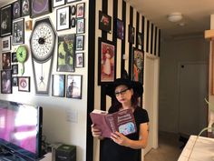 a woman standing in front of a wall with pictures on it and holding a book