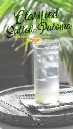 a glass filled with liquid sitting on top of a metal tray next to a palm tree