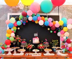 a table topped with lots of cake and desserts covered in balloons, flowers and confetti