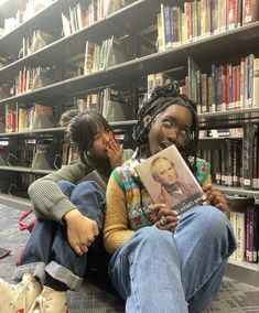 two children sitting on the floor in front of bookshelves with one holding a book