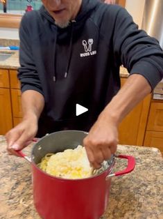 an old man is preparing food in a red pot on the kitchen counter, and he is holding a ladle