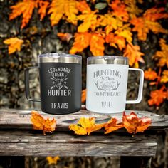 two stainless steel mugs sitting on top of a wooden table next to autumn leaves