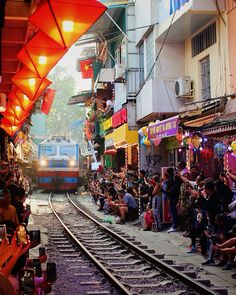 people sitting on the side of train tracks as a train passes by in front of them