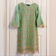 a green and gold dress hanging on a white door with an ornate design in the middle