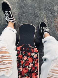 a person standing next to a skateboard with flowers on the board and ripped jeans