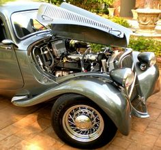 an antique car with the hood open and engine in it's trunk, parked on a brick driveway