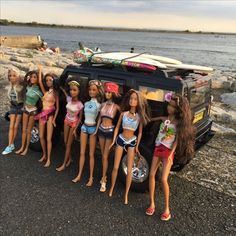 a group of barbie dolls standing in front of a car