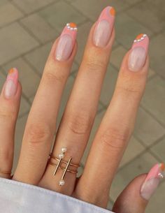 a woman's hand with pink and white nail polish holding a cross shaped ring