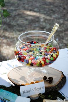 a glass bowl filled with candy sitting on top of a wooden slice next to a sign