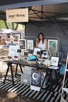 a woman standing in front of a table with pictures on it at an outdoor market