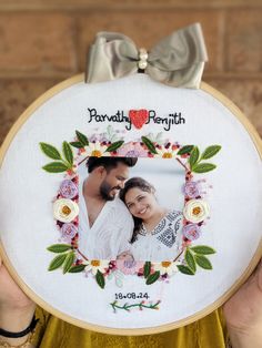 a man and woman holding up an embroidered photo frame