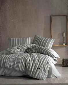 an unmade bed with grey and white striped comforter in a gray room next to a mirror