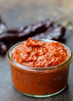 a jar filled with red sauce sitting on top of a table next to dried peppers