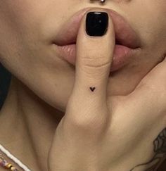 a close up of a person with a finger on her nose and a heart tattoo