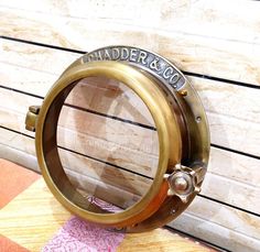 a brass porthole with the name chandler & co on it sitting against a wooden wall