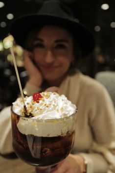 a woman sitting at a table with a drink in her hand and whipped cream on top