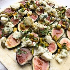 a pizza with figs, cheese and pistachio on it sitting on a cutting board