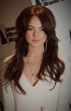 a woman with long dark hair wearing a white sweater and diamond necklace, posing for the camera