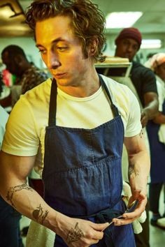 a man with tattoos on his arm and an apron around his waist holding something in his hand