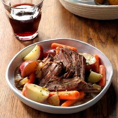 a bowl filled with meat, potatoes and carrots on top of a wooden table