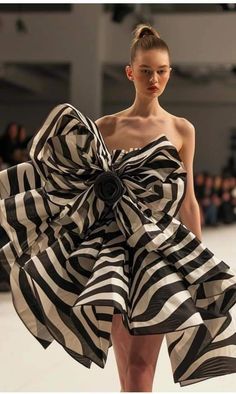 a woman is walking down the runway wearing a dress with large, black and white stripes