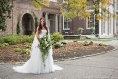 a woman standing in front of a brick building holding a bouquet of flowers and greenery