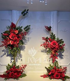 two red flowers and greenery on display in front of a white wall with chandelier