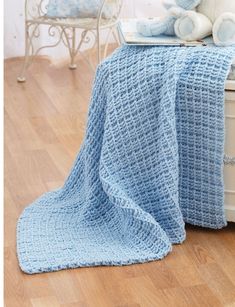 a blue crocheted blanket sitting on top of a bed next to a teddy bear