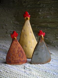 three ceramic roosters sitting on top of a bed next to each other in different colors