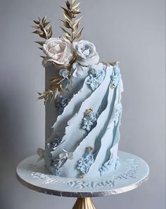 a blue and white cake with flowers on top is sitting on a gold plated stand