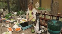 a woman standing in front of a table filled with vegetables and fruit on top of it