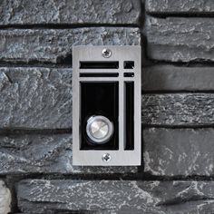 an electronic device mounted to a stone wall with a metal button on the left side