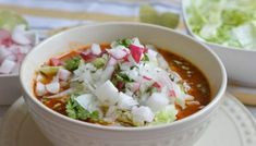 a white bowl filled with soup next to another bowl full of salad and lettuce