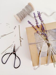 scissors, twine and lavender sprigs are on the table next to a wrapped gift