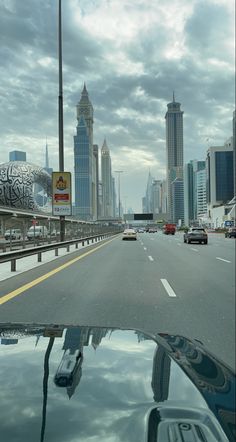 cars driving down the road with tall buildings in the backgrouds and cloudy skies