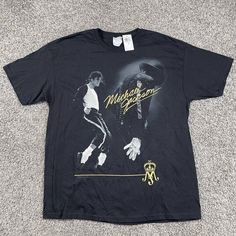 a black michael jackson t - shirt sitting on top of a gray carpeted floor