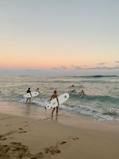 several surfers carrying their surfboards into the ocean at sunset or dawn on an empty beach