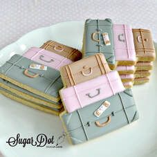 four pieces of luggage cookies are on a white plate with pink and blue trimmings