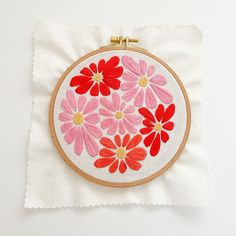 a red and pink flower embroidered onto a white piece of cloth with a gold frame