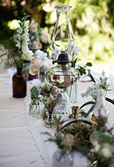 several vases filled with flowers and greenery on a white table cloth covered table