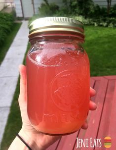 a person holding up a mason jar filled with liquid on a wooden deck in front of a house