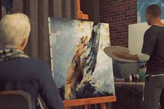 an older man holding a white frisbee in front of a painting on easel