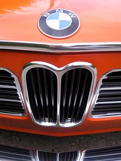 an orange bmw emblem is shown on the front of a red car with chrome grills