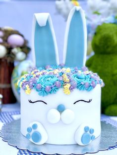 a white cake with blue frosting and flowers in the shape of a bunny's face