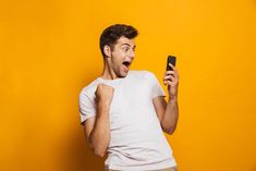 a man holding a cell phone in his right hand and making a funny face while standing against a yellow background